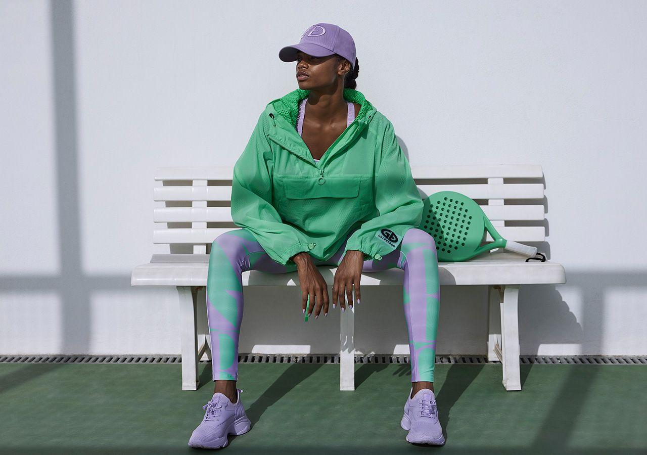 Femme assise sur un banc, vêtue d'une veste de tennis verte à la mode