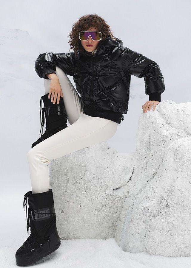 Seated woman in white trousers, jacket, glasses and high snow boots