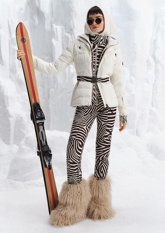 Woman in fashionable ski outfit holding skis leaning on the ground