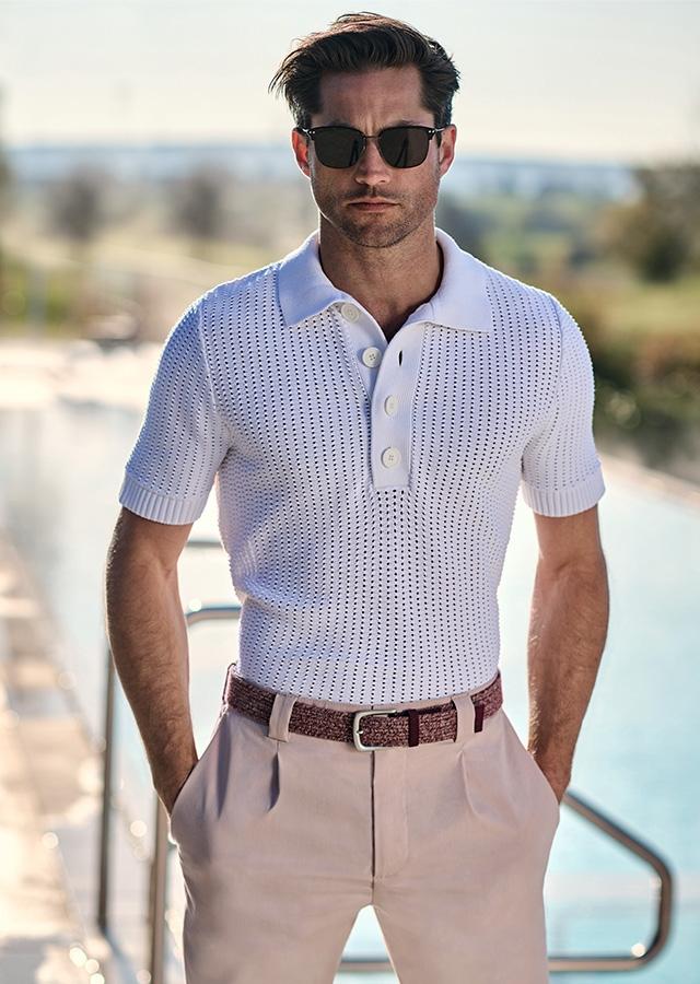  Mężczyzna w stylizacji w duchu office core – białej polówce i beżowych spodniach z brązowym paskiem   